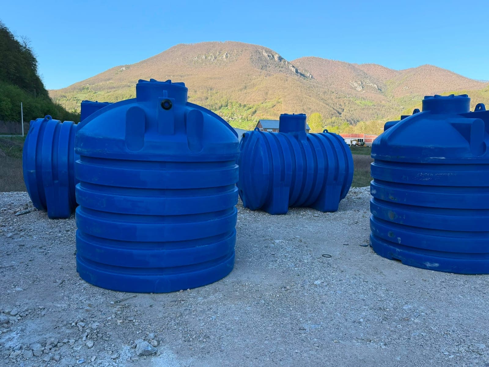 Vertikalni i horizontalni plastični rezervoari na platou, planina u pozadini